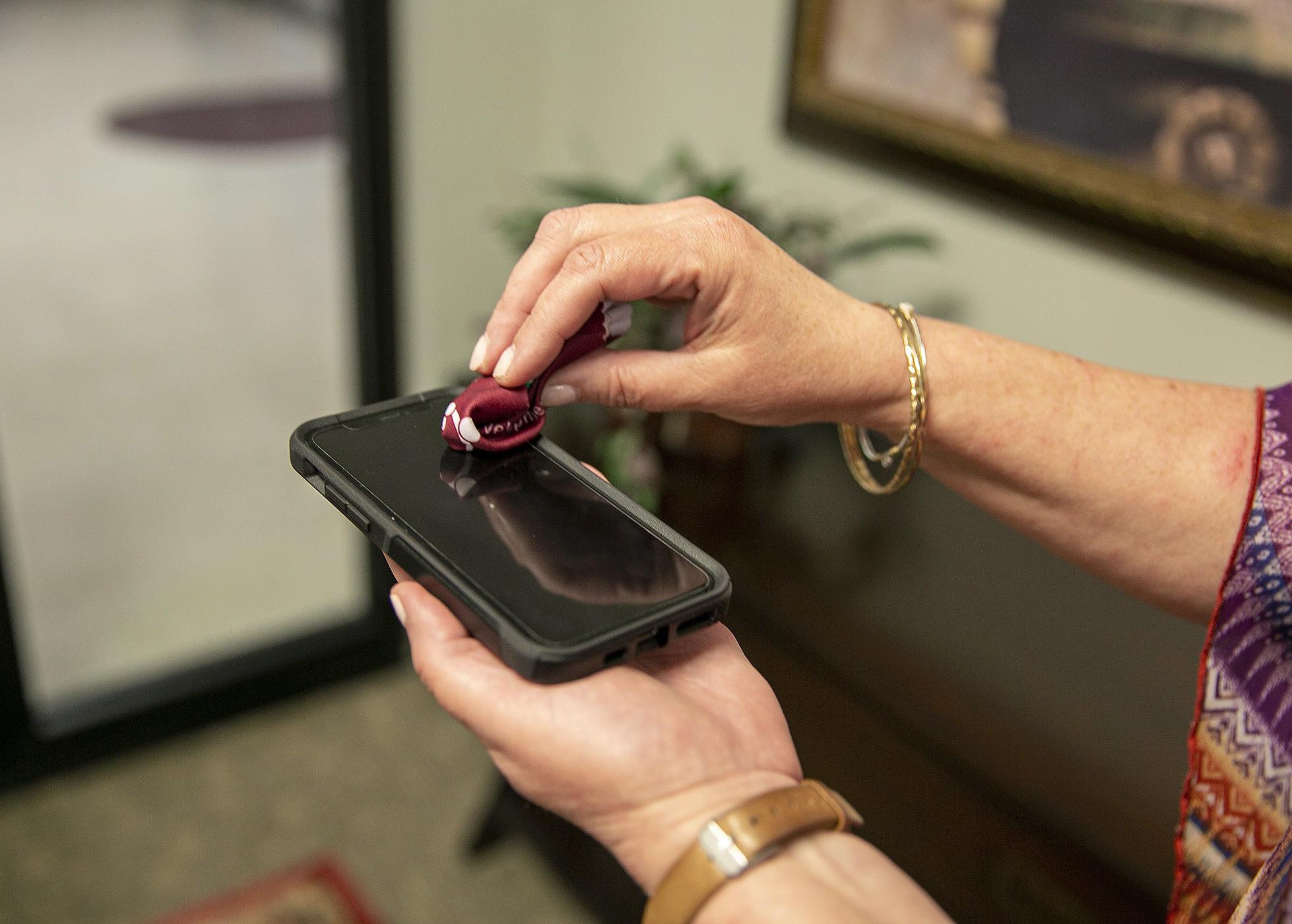 One hand holds a phone while the other hand wipes the screen with a small cloth.