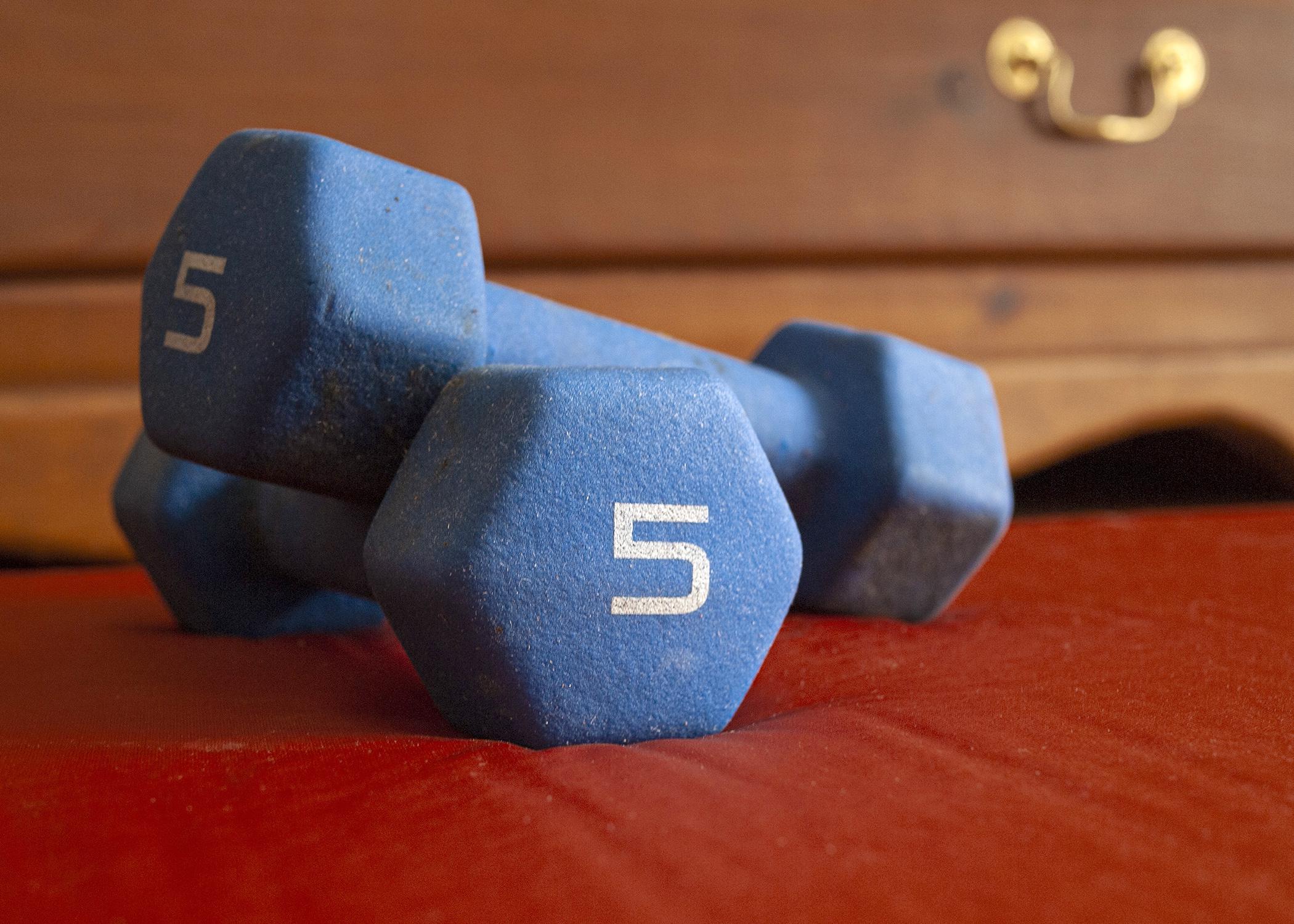 Two blue dumbbells are stacked on a bedroom floor.