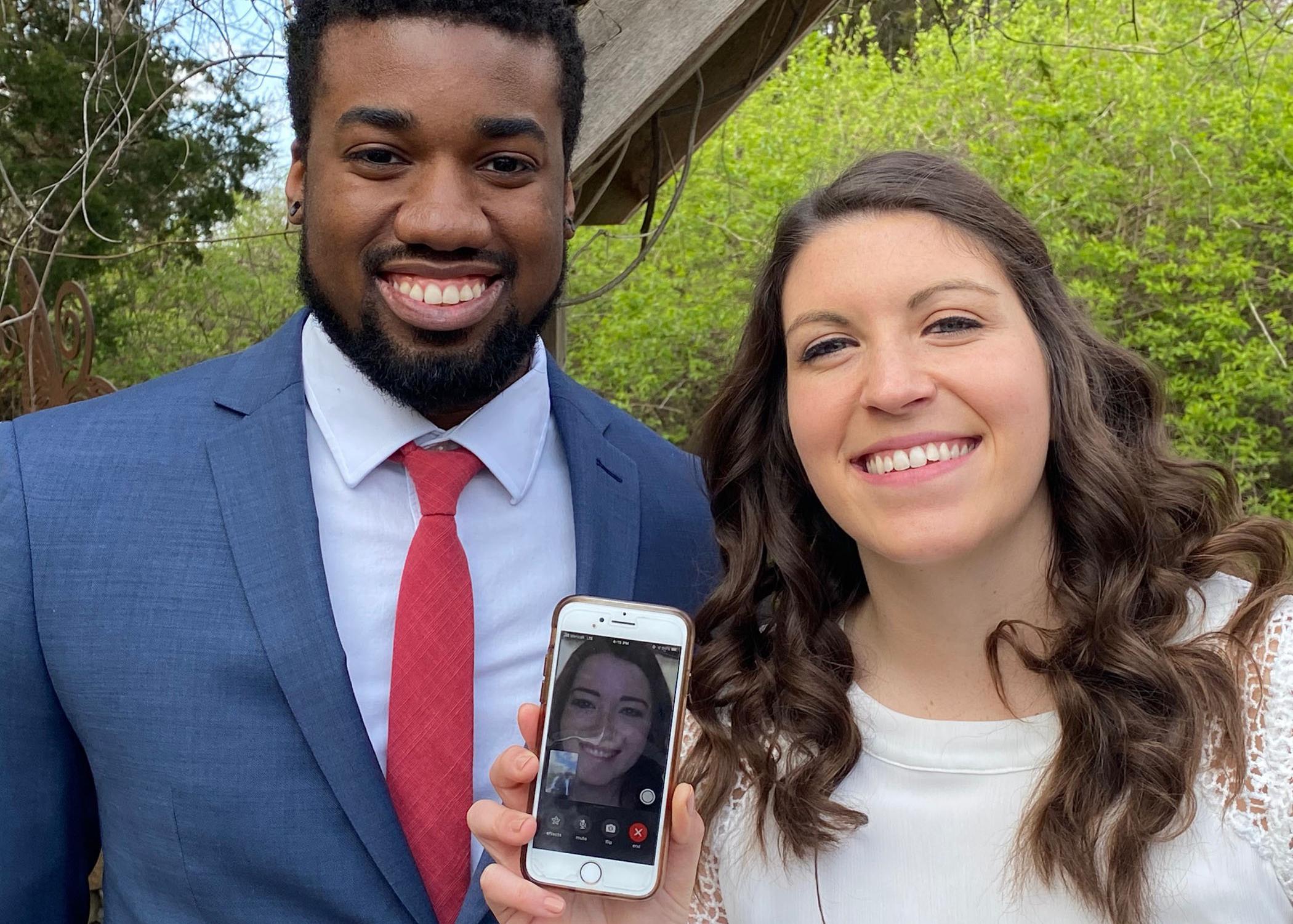 A smiling couple holds a smart phone showing a woman on a video call.