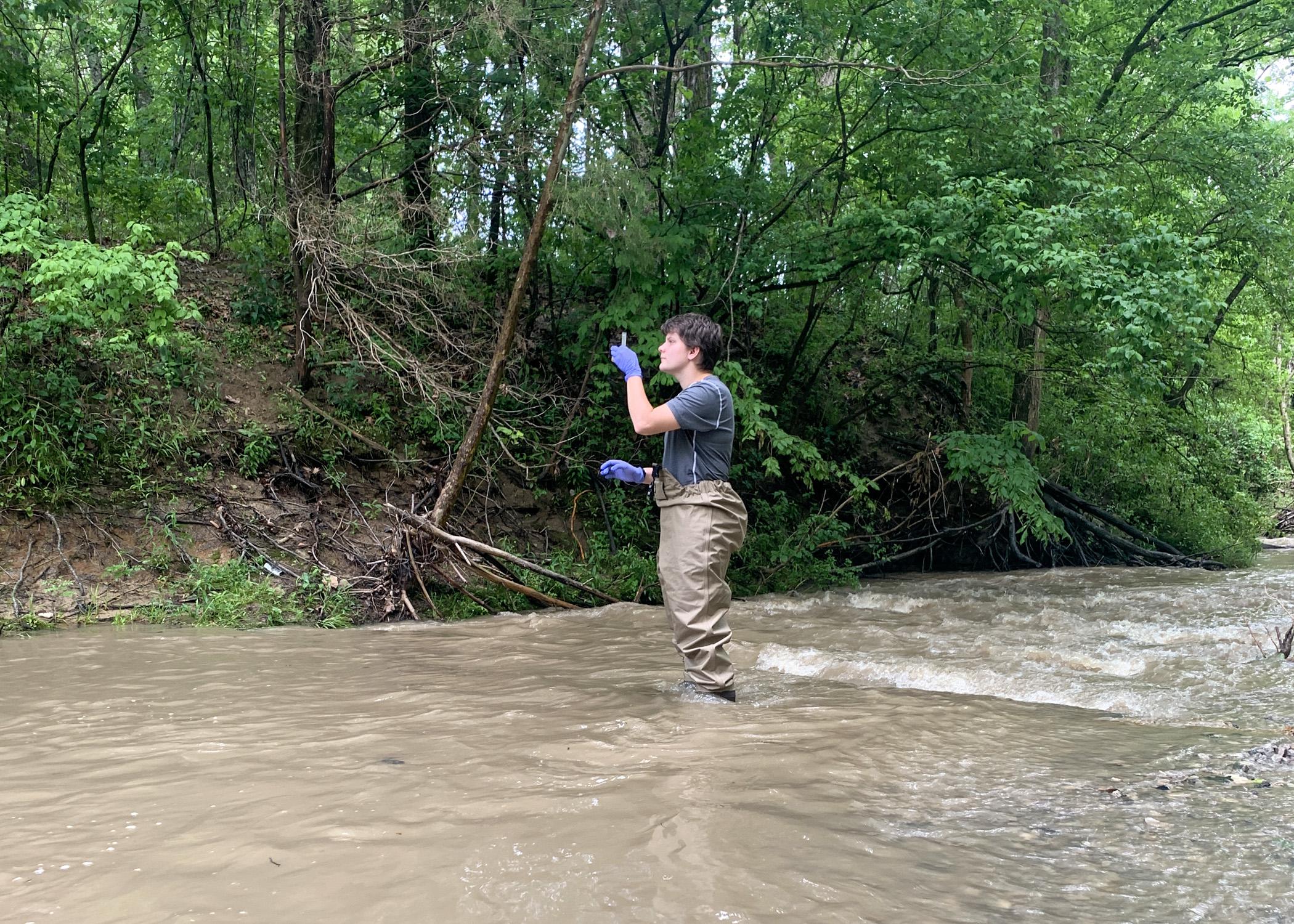 Woman in wading pants collects a water sample in a creek.