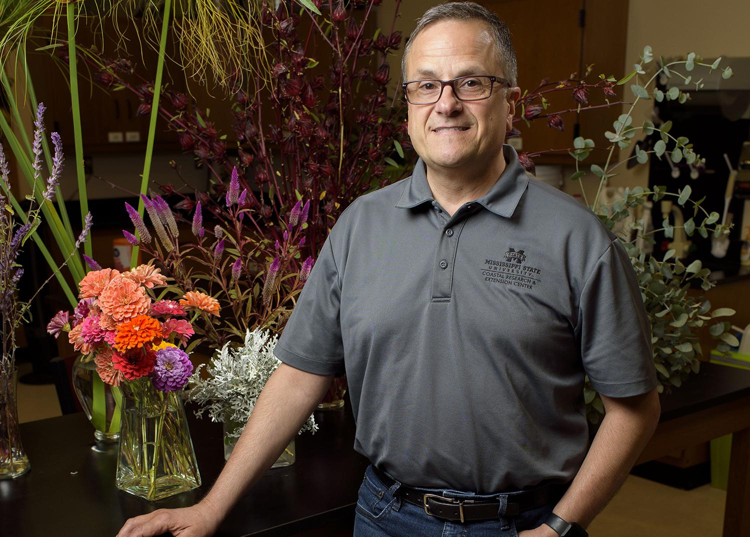 A man stands at a table holding floral arrangements.