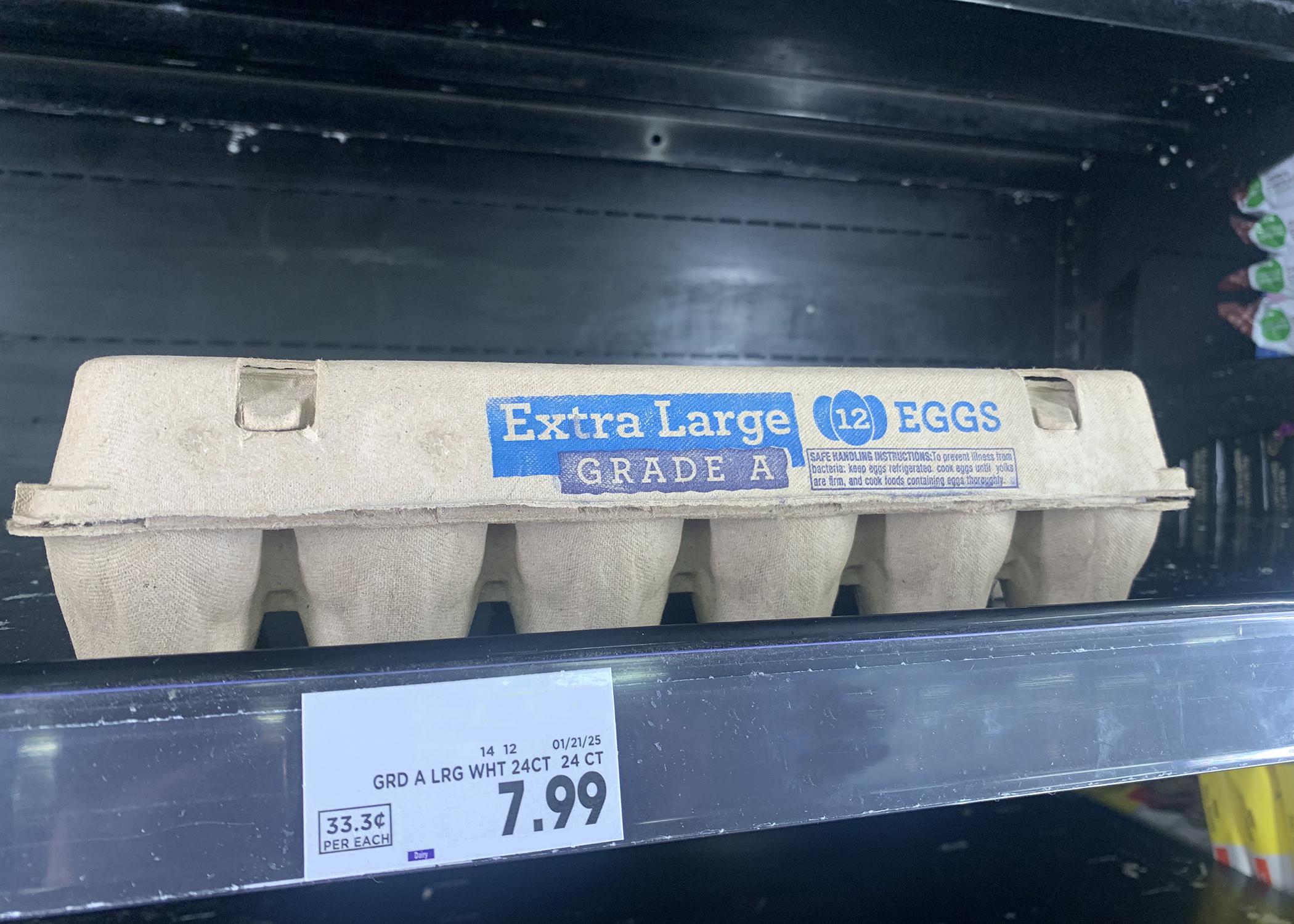 A carton of eggs on a grocery store shelf with an affixed price tag.