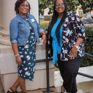 Two women standing in front of a column, smiling.