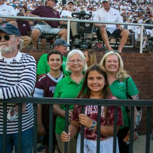 Two women standing outside and wearing green shirts smiling behind a girl wearing a maroon shirt.