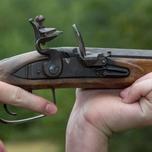 A close-up image of a flintlock rifle’s hammer and trigger.