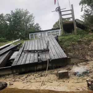 An old wooden dock that has fallen onto a sandy bank at the edge of the water.