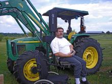 Chris Bell sits next to his tractor that has been equipped with a lift device and hand controls so he can operation it from his wheelchair. (Photo by Emily Knight/Mississippi State University Extension Service) See larger view.