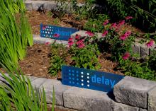 Blue signs stating “absorb” and “delay” mark brick tiers in a landscape growing pink flowers and reed-like stems.