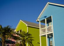 Palm trees adorn the landscape in front of blue, green and pink cottages.