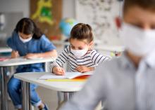 Three students wear face masks as they sit at their desks.