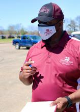 Man in maroon shirt and cap with a clipboard and pen.