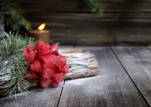 A red bow rests on a log with evergreen foliage in front of a candle.