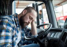 Tired man rests his head in a truck cab.