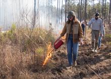 A woman starts a controlled fire in the woods with a group of people.