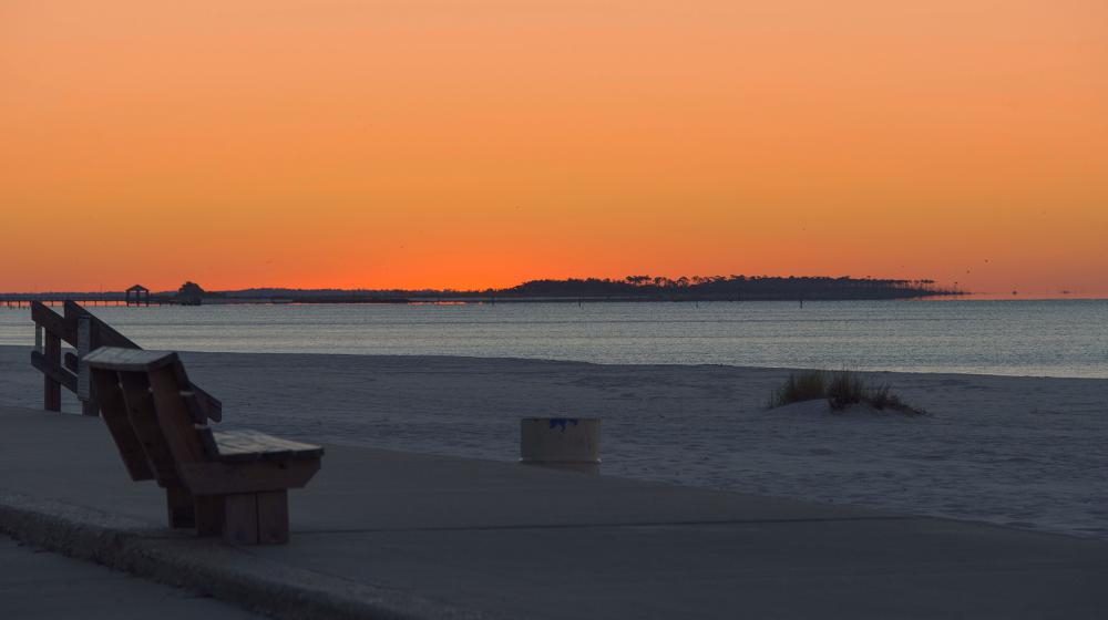 An orange sunset on Biloxi beach with the Gulf of Mexico in the background.