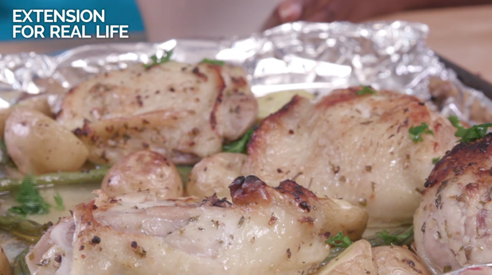 Several browned bone-in chicken thighs on top of halved baby potatoes and green beans on a foil-covered sheet pan.