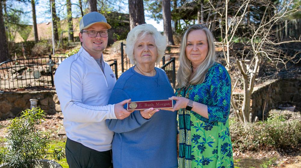 A woman, flanked by a young man and woman, holds a nameplate listing “E. Ruth Morgan.”