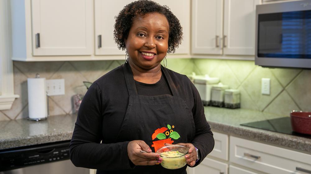 A woman stands in a kitchen and holds a bowl of soup.