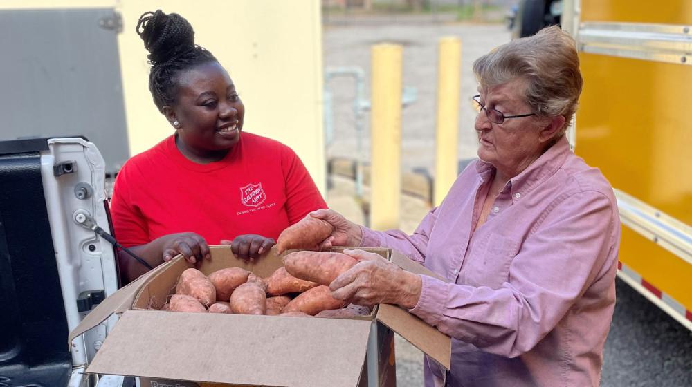 Two women with a box of sweet potatoes .