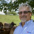 A man wearing a light blue shirt with “US Jersey” above the chest pocket stands smiling in front of several cows.