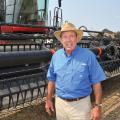 A man wearing a blue shirt and cowboy hat stands in front of a piece of farming machinery.