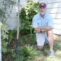 A man kneels in a flower bed next to some plants. 