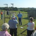 A group of adults gather outside a metal corral with electronics attached to it with a speaker inside the trap.