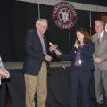 Woman handing man silver cowbell and shaking his hand.