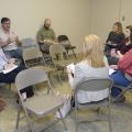 Man in glasses speaking to a group of people sitting in a circle.