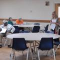 Blonde-haired woman with glasses in a large room speaking to a group of farmers.