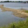 Flood water covers a field except for an elevated dirt path leading to a house in the background.