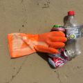 Small pile containing a rubber glove, an empty plastic bottle and two aluminum cans on wet sand.