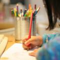 A child uses a colored pencil to write on a sheet of paper.