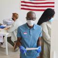 Voter wearing mask, standing by booth and looking at camera.