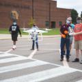 A drone in the foreground being controlled by young students in the background.