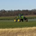 A tractor with a spray rig crosses a wheat field.