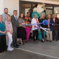 A group of people hold a ribbon in front of a building entrance.