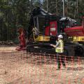 A man wearing a hard hat talking into a microphone in front of a piece of heavy equipment.