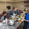  adult instructs two children in a kitchen setting.