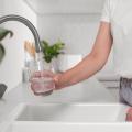 A person fills a glass with water at a kitchen sink.