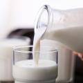 Hand pours milk from a glass bottle into a cup