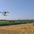 A large drone hovers over cropland.