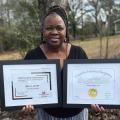 A woman holds two framed certificates.