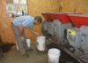 Man leans over a 5-gallon bucket placed under a large mechanical unit inside a building.