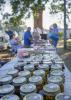 Rows of canning jars line a table at an open-air marketplace.