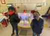 Two children in masks stand in front of an activity center in a classroom.