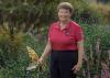 A woman holding a gardening tool stands in a green landscape.