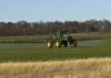 A tractor with a spray rig crosses a wheat field.