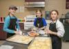 Three girls work with dough sheets at a table.